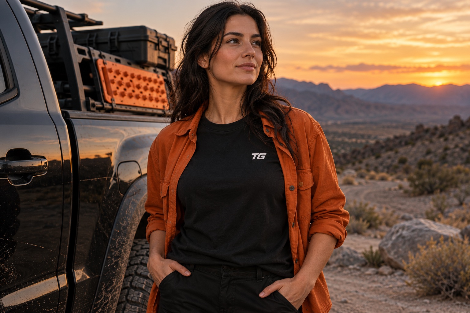 Adult woman in a TG tee and orange overshirt beside a pickup at a desert trailhead