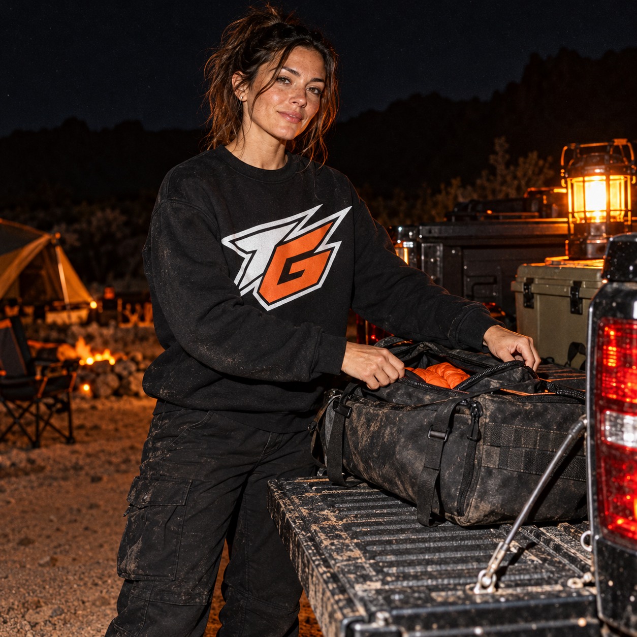 Adult model in a TG sweatshirt packing gear on a coated pickup tailgate at night